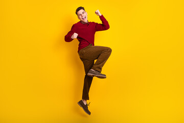 Fototapeta na wymiar Positive Young Handsome Man in Red Sweater Jumping Joyfully Against Yellow Background