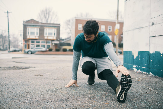Man stretching before workout on urban sidewalk during rainy day