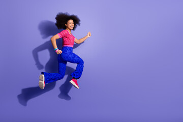 Young woman in stylish retro outfit jumping joyfully against vibrant violet background in a dynamic pose