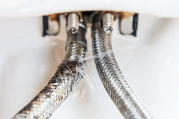 The faucet connection hoses, one of which is burst and water is coming out of it under pressure.