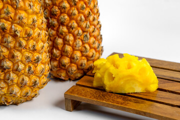 Closeup of fresh ripe pineapples with peeled slice on wooden board and white background. Tropical exotic fruit for healthy food, summer snacks, or natural product advertising.