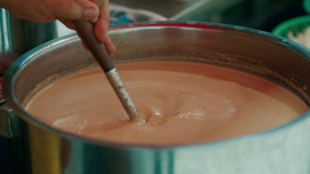 Detailed close-up of a hot soup being stirred in a metal pot at a street market. Captures the cooking process and texture of the creamy broth.