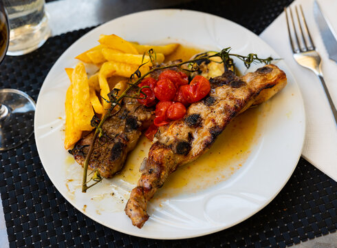 Spanish dish Churasko - barbecue ribs, complemented by baked tomatoes and eggplants. Glass of red wine and glass of cool refreshing water are served with dish..