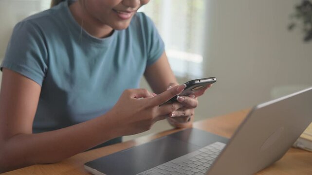 Young adult female black asia people happy relax work at home enjoy play typing ask chat bot mobile phone buy or paying order retail app generative AI chatbot. Playing chatGPT robot search text data.