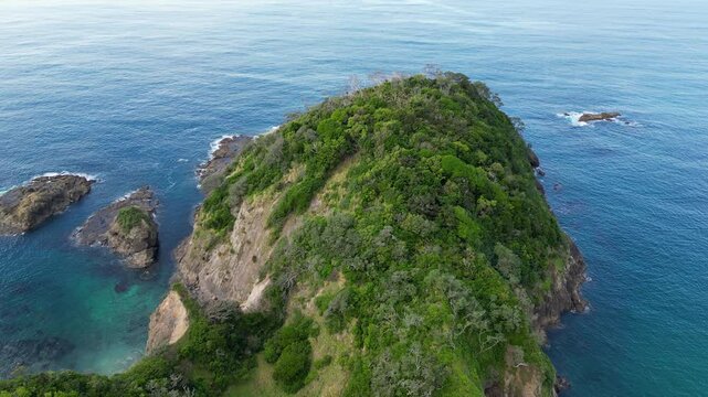 Drone view of a rugged headland rising from turquoise waters with natural vegetation along New Zealand&rsquo;s coastline. Matapouri.