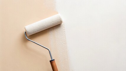 Obraz premium A white paint roller with a classic wooden handle smooths a fresh coat of white paint onto a beige wall, creating a crisp, diagonal line of transformation