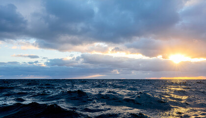 Obraz premium Dramatic Ocean Waves at Sunset with Cloudy Sky and Golden Light Reflection