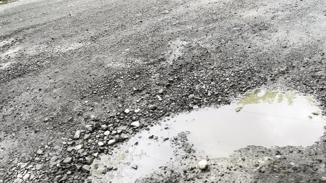 Potholes and holes filled with water. A bad broken road with a destroyed surface and large holes. A road in need of repair.