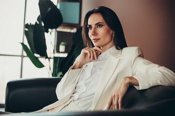 Confident businesswoman in elegant white suit sitting in modern office environment, deeply...