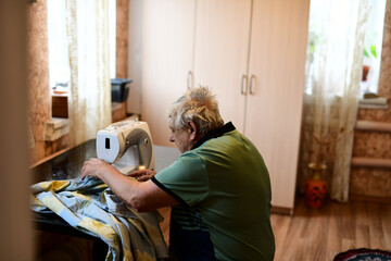 An elderly man of retirement age sews clothes on an electric sewing machine