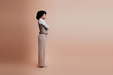 Elegant young businesswoman in formal attire posing confidently against a beige studio background,...