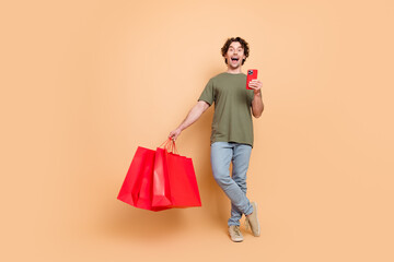 Young man with shopping bags and smartphone enjoying online shopping against beige background