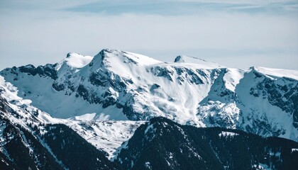 Obraz premium Snow-covered mountain peaks under a partly cloudy sky, trees visible below