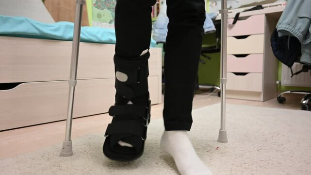Child with Broken Leg Uses Crutches and Walking Boot in Bedroom