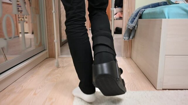 Person with Injured Foot Walks at Home Using Crutches and Orthopedic Boot