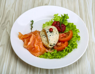 A beautifully arranged plate featuring smoked salmon, fresh vegetables, and a creamy cheese on a wooden table