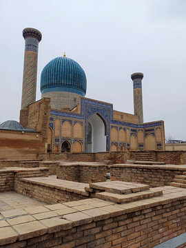 Gur-e Amir mausoleum in Samarkand, Uzbekistan. The building features a large, ribbed blue dome and two tall minarets, showcasing Timurid architecture. The facade is adorned with vibrant blue and white