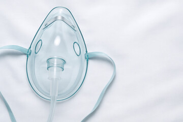 Oxygen Mask on Bed Sheet: A clear plastic oxygen mask with elastic straps lies on a smooth white bed sheet, ready for use.  The image conveys a sense of medical care and breathing support.