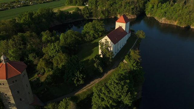 Cinematic aerial shot of the Wehrkirche Beucha on a rocky cliff above a quarry lake at sunset near Leipzig, Germany. Highlights historic architecture, dramatic terrain, and serene evening light.
