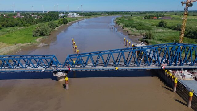 Drone shot of the Friesenbr&uuml;cke railway bridge in closed position over the River Ems. Captures the steel structure, muddy river, and flat countryside on a clear summer day during the building phase.