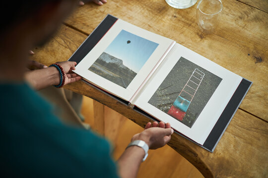 Person looking at opened photo album with travel pictures including landscape and colorful steps on wooden table with glass