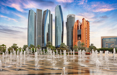 Fototapeta na wymiar Skyscrapers in Abu Dhabi at dramatic sunset with fountain; United Arab Emirates