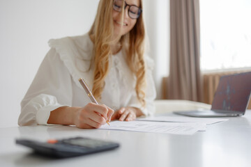 Young woman working on documents at a desk with a laptop and calculator in a bright office space during the day