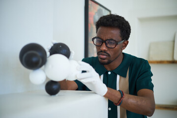 African American man wearing glasses deeply focusing on adjusting a molecular model in a modern lab...