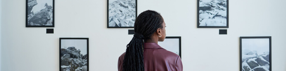 Header with woman with long braids facing black-and-white photograph gallery wall deeply observing...