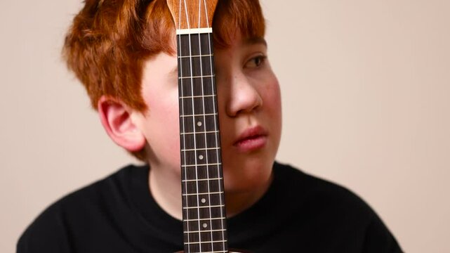 one boy in a black shirt plays the ukulele closeup, a little boy with red hair plays the ukulele musical instrument, side view