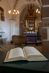 An open holy book rests at the front, gazing out over the church, where the chandelier glimmers above the nave