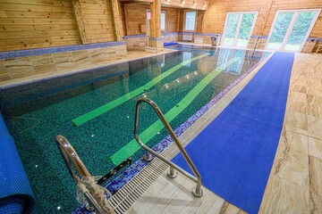 Indoor pool with wood paneling and tiled floor. Features a blue runner alongside the pool and...