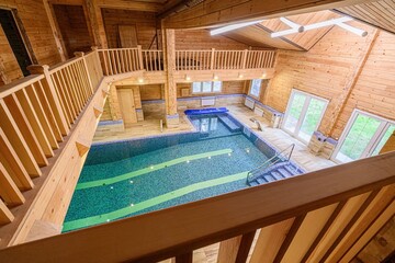 indoor swimming pool is surrounded by wooden walls and railings in a multi-level house. The pool is tiled and includes green lines and steps. Large windows provide natural light