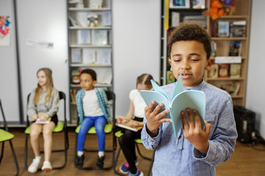 Young boy reads a book aloud during classroom activity in cozy learning environment. Back to school