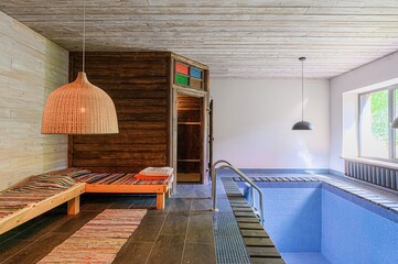 Indoor pool room with a sauna, lounge area with a woven lamp, and a tiled pool with a ladder....