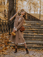 Beautiful blonde young woman in hat and coat walking on the stairs in the autumn park.