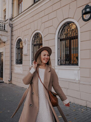 Beautiful young woman in hat and coat walking around european city