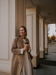 Young girl smiling and standing with coffee in her hands near a column in the city