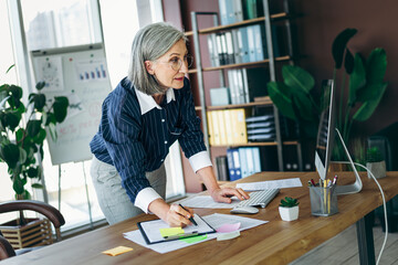 Mature businesswoman working in a modern office, reviewing papers and using a computer with a focused and professional approach