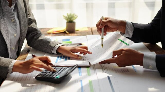 Young colleagues discuss business and analytical price charts using calculators and laptops to calculate financial, tax, accounting, statistics and analytical research ideas.