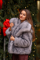 Beautiful Caucasian girl on the street in winter in a fur coat celebrates Christmas and New Year.