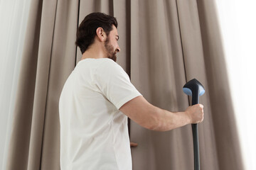 Man steaming curtains with stand steamer at home