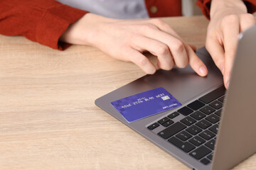 Online payment. Woman with credit card typing on laptop at wooden table, closeup