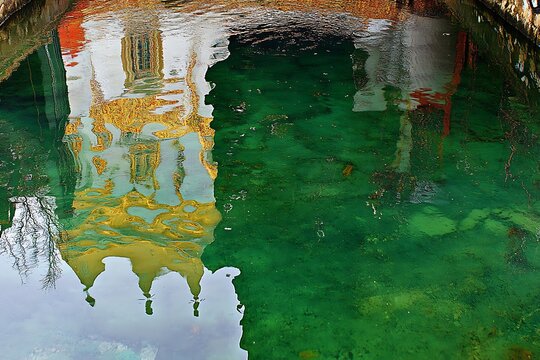 Reflection of vibrant buildings in a serene green canal water with visible ripples and a glimpse of the surrounding architecture