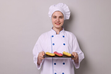 Confectioner in uniform holding delicious eclairs on light grey background