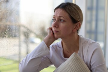 Depressed woman near window at home, space for text