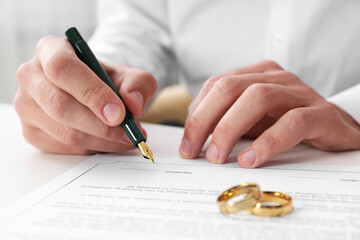 Man signing marriage contract and wedding rings on desk, selective focus