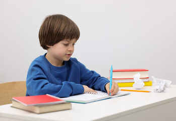Cute little boy doing homework at desk indoors