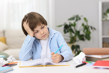 Tired little boy doing homework at table indoors