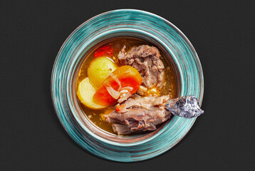 Top-view photograph: a bowl of flavorful broth-based lamb soup with potatoes, carrots, and onions,...